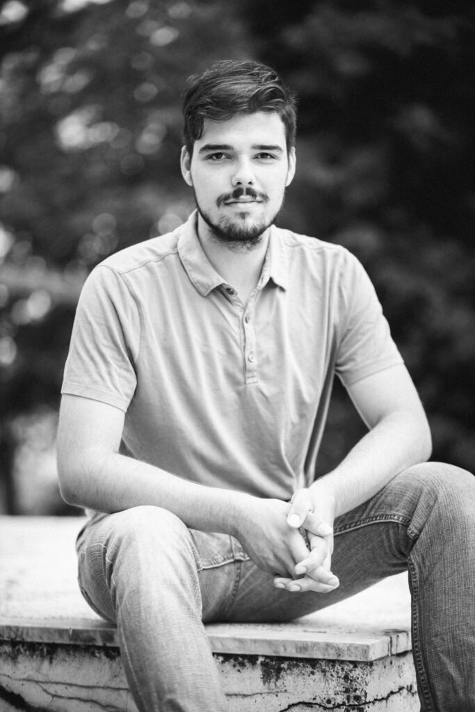 A grayscale shot of a young Caucasian male wearing jeans and a t-shirt sitting on a bench