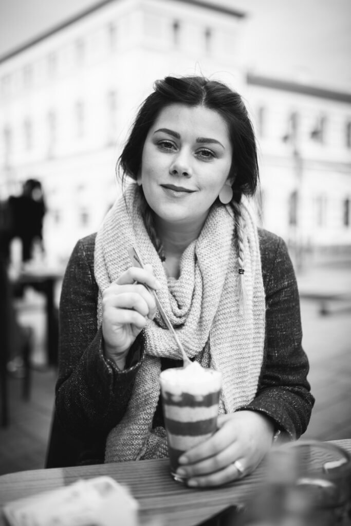 A greyscale portrait of a pretty smiling girl eating chocolate dessert from the cup on the street cafe